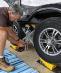 Man using Curved Camper Leveler And Wheel Chock For RVs And Trailers Up To 30,000 Lbs By Camco under tire, drive on leveling