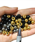 Hand holding assorted M4 thread cap nuts including silver steel ball screw caps for furniture lighting, smooth metal finish.