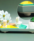 Decorative tray with geometric sections, flowers, mini busts, and succulent. Round inset shows close-up of tray's rounded feet.