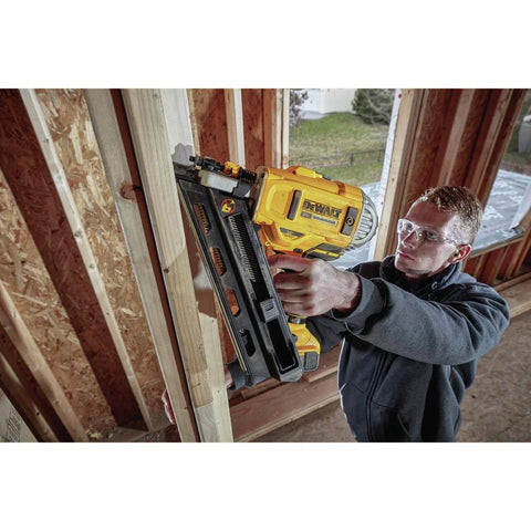 Man using DEWALT 20V MAX XR Framing Nailer to drive nails into a wooden frame on a construction site