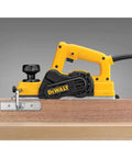 Side view of DEWALT 3-1/4 Inch Hand Planer Kit with a 5.5 Amp motor, trimming wood with carbide blades for precise edge shaving.
