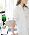 Digital Hydrogen Meter Water Quality Tester with ATC and Data Hold Function measuring water in a glass beside a woman drinking.