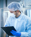 Person wearing white disposable lab coat for adults, medium size, 40 GSM polypropylene, with hair net and mask, holding a clipboard.