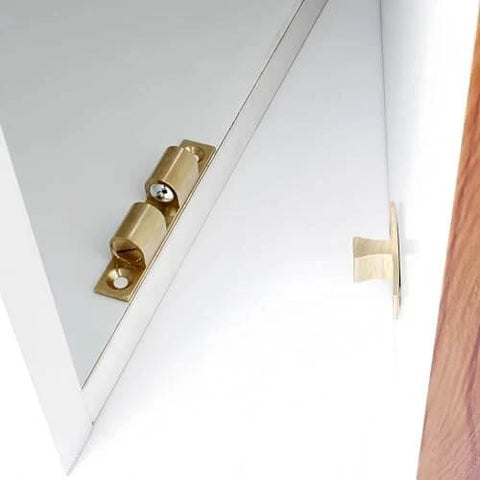 Brass spring detent latch on white cabinet door, angled view for precise positioning, indexing, locking in mechanical equipment.