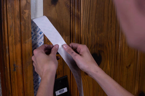 Person applying Double Sided Containment Tape for Painting and Remodeling to wooden door frame, natural color, 48 mm by 23 meters.