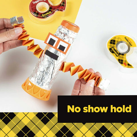 Hands holding a robot craft made with foil and colored paper, shown with double sided tape rolls for gift wrapping and crafts.