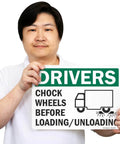Person holding Chock Wheels Before Loading And Unloading Sign For Drivers, 10 By 14 Inch Aluminum, Heavy Duty Rustproof Outdoor Safety Sign With Four Corner