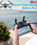 Hands holding drone remote control with a screen, view of flying area. Ensure fully charged before flying note visible.