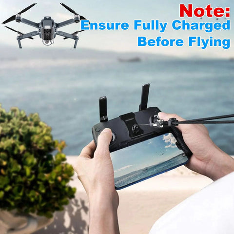 Hands holding drone remote control with a screen, view of flying area. Ensure fully charged before flying note visible.