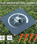 Foldable 22 Inch Drone Landing Pad With Fast Fold System 2x3 Double Sided Waterproof Launch Pad Weighted Helipad Blue Gray Durable Universal Pad for Mud Sand Snow Easy Rinse Clean Ready shown with drone on grass and ground anchors
