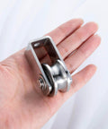 Person holding dual-bearing cable pulley wheel set for rope systems, wall or ceiling mounted, stainless steel construction