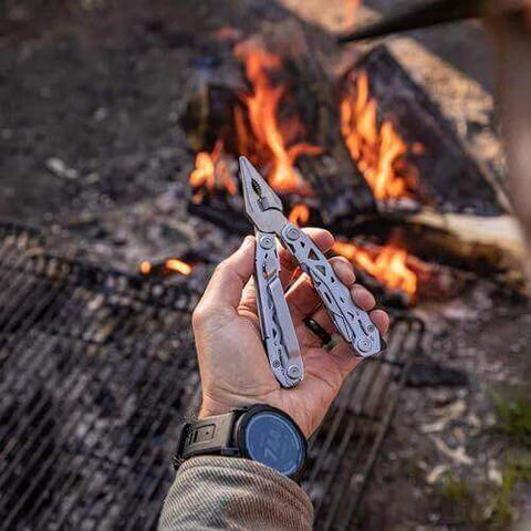 Man holding Suspension-NXT 15-In-1 EDC Multi Tool With Pocket Knife, Needle Nose Pliers And Wire Stripper by a campfire
