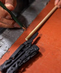 Person using Suspension-NXT 15-In-1 EDC Multi Tool with pocket knife and pliers, next to a pencil and wooden dowel on a workbench.