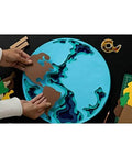 Hands assembling a globe puzzle with brown pieces on a table with scissors and tape. Product in the background is Double Sided Tape For Gift Wrapping And Crafts, Snaps On Quick For Holiday Gift Wrap, Bags, Scrapbooking And School Projects, 0.75 Inch Wide By 1296 Inch Length, Two Refill Rolls For Clean, Mess Free Bonding.
