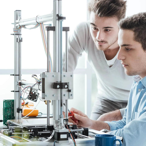 Two people working on a 3D printer in a bright room, focusing on assembly and adjustments.