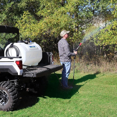 Person using Everflo 12V On-Demand Diaphragm Sprayer Pump - 5.5GPM, 60 PSI, Quick Attach Ports on a utility vehicle to spray trees
