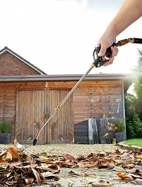 Extendable air blow gun with a 19 to 28 inch nozzle, blowing leaves in front of a wooden shed, visible hand holding the tool.
