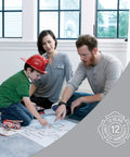 Family sitting on floor discussing fire safety plan, fire truck toy, and blueprint in home setting; 12-year limited warranty badge visible.
