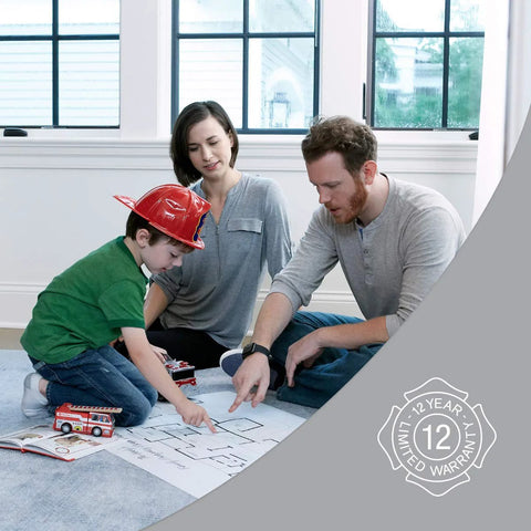 Family sitting on floor discussing fire safety plan, fire truck toy, and blueprint in home setting; 12-year limited warranty badge visible.