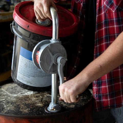 Person operating Fill-Rite SD62 Hand Pump Rotary 2-Vane Curved Spout on a drum for fluid transfer in an industrial setting.