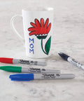 Fine point permanent markers deliver bold, precise lines with quick-drying, odorless ink used on a mug and scattered on a table.