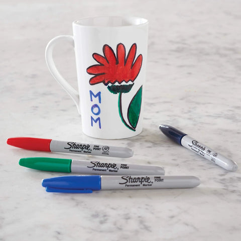 Fine point permanent markers deliver bold, precise lines with quick-drying, odorless ink used on a mug and scattered on a table.