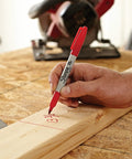 Fine point permanent marker with red ink drawing bold, precise lines on a wooden plank in a workshop setting.