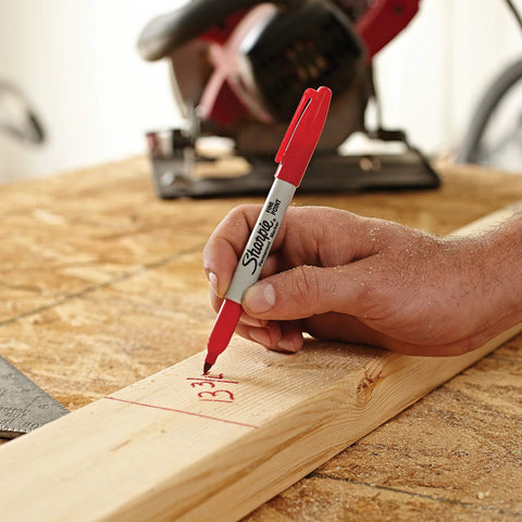 Fine point permanent marker with red ink drawing bold, precise lines on a wooden plank in a workshop setting.