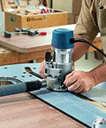 Woodworker using Fixed Base Router 2.25 HP 12 Amp Variable Speed 8000 to 25000 RPM for precise edge work on a table.