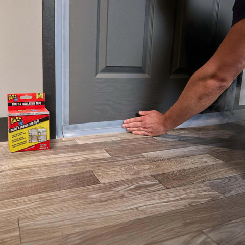 Applying Flex Seal Draft and Insulation Sealing Tape, 2 in x 16 ft, clear rubberized strip to door; pack visible beside hardwood floor