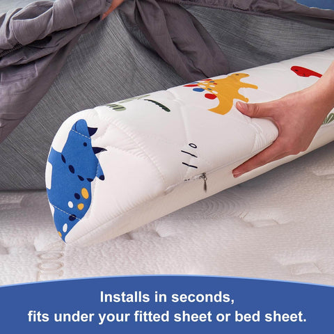 Toddler bed bumper with dinosaur print being placed under gray bed sheet; 2 Pack Premium Foam Toddler Bed Bumpers With Non Slip Rails For Twin Queen And King Beds Cozy Odor Free Comfort Machine Washable Covers Easy Care 52 By 7 By 5 Inches Safe Sleep Aid For Peaceful Nights.