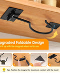 Close-up of an upgraded black magnetic foldable hook under a shelf with instructions for positioning the magnet for maximum contact.