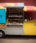 Food truck with open concession shelf displaying various snacks and condiments on a sunny day.