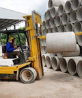 Forklift with 84 Inch Fork Extensions For Forklifts in use lifting concrete pipe at a construction site.