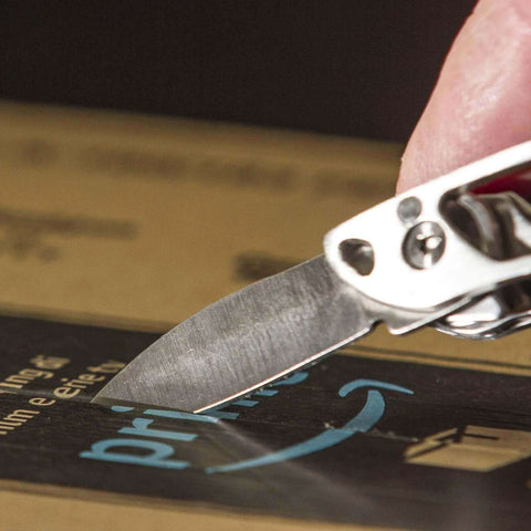 Close-up of Framework Mini 11 In 1 Multitool knife cutting a cardboard box, highlighting precision and compact design for everyday use.
