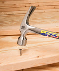 Framing Hammer 28 Oz Long Handle Straight Rip Claw With Milled Face And Shock Reduction Grip For Superior Leverage, Reduced Hand Fatigue, Precise Striking Power On Framing And Heavy Duty Carpentry, USA Made One Piece Forged Steel Construction E3 28SM hammer driving nail into wood.