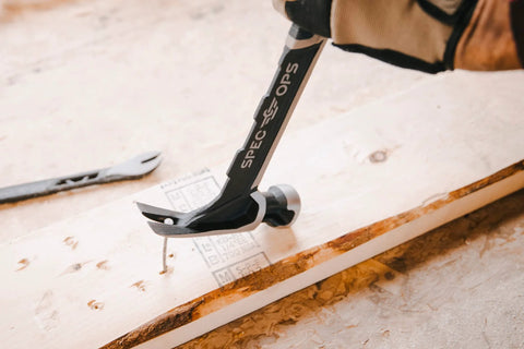 Framing Hammer 22 Oz Rip Claw Smooth Face With Shock Absorbing Grip Ballistically Balanced For Framing Demolition And Nail Setting On Tough Job Sites Plus Three Percent Donated To Veterans being used to pull a nail from wood surface.