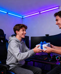 Two people in a gaming setup exchanging a wrapped gift, surrounded by computer screens and gaming peripherals.