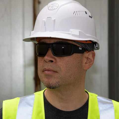Man wearing full frame gasket safety glasses with foam seal, anti-fog, UV scratch-resistant, and hard hat in industrial setting.