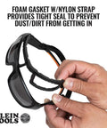 Hands holding full frame gasket safety glasses with foam seal and nylon strap, anti fog UV scratch resistant features.