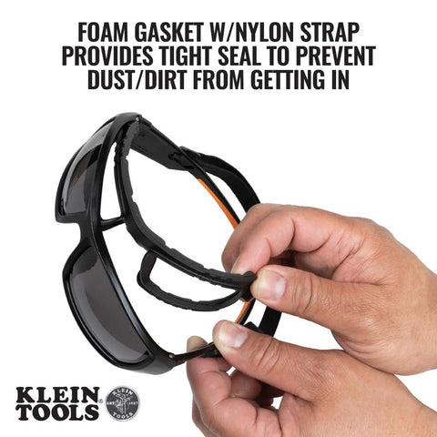 Hands holding full frame gasket safety glasses with foam seal and nylon strap, anti fog UV scratch resistant features.