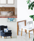 Home interior featuring wooden furniture, a blue armchair, a wooden sideboard, and a white chair with a table amidst green plants.