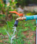 Outdoor water faucet with orange handle and flowing water, attached with a 3/4 inch garden hose quick connector set adapter.