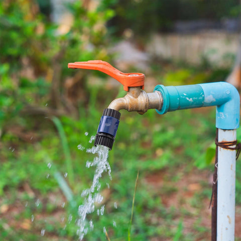 Outdoor water faucet with orange handle and flowing water, attached with a 3/4 inch garden hose quick connector set adapter.