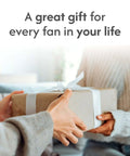 Hands exchanging a gift box with text "A great gift for every fan in your life" in cozy room setting