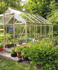 Glass greenhouse in a garden setting with plants around and inside, showcasing outdoor cultivation.