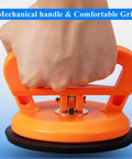 Close-up of hand holding Two Pack Glass Vacuum Suction Cups Lifter Dent Puller Tool, orange handle with rubber chassis for glass surfaces