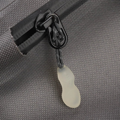 Close-up of glow-in-the-dark zipper pull on grey fabric, part of the 3 In 1 Nylon Zipper Puller Replacement Pack For Backpacks And Clothing.
