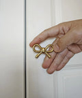 Hand holding a gold vintage bow-shaped drawer knob against a white door, part of the 2 Pack Solid Brass Bow Drawer Knobs In Gold.