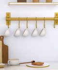 Kitchen Utensil Holder Hanger, Pot and Pan Rack Wall Mounted, gold, with 8 hooks holding mugs, mounted on kitchen wall.